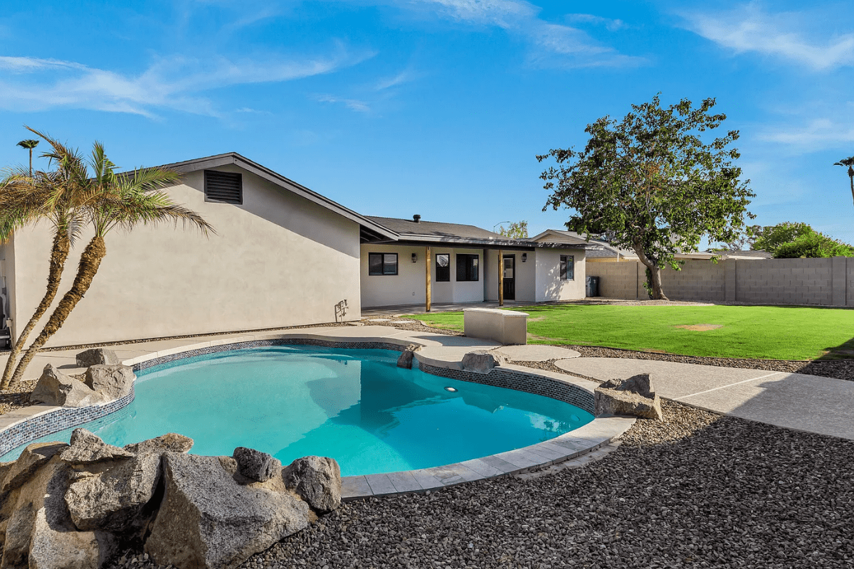 Backyard with a small pool, palm tree, and grass area next to a single-story house.