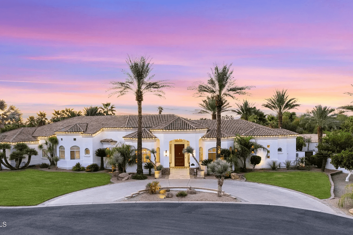 Large white villa with palm trees, under a vibrant pink and purple sunset sky.