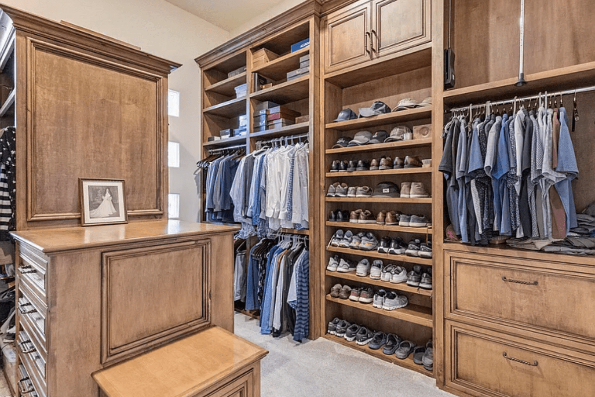 Spacious walk-in closet with wooden shelves, neatly organized clothes, shoes, and a framed photo.