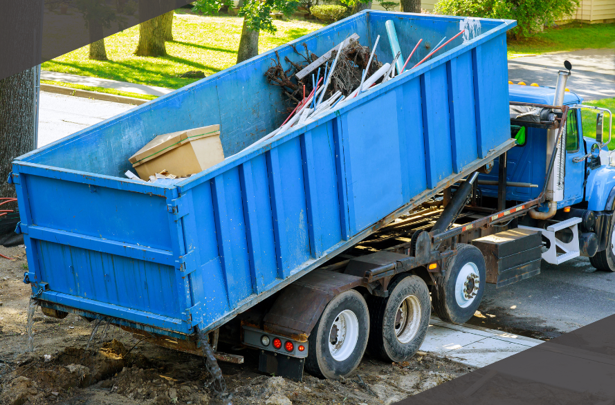 Dump truck unloading construction debris into a blue container on a residential street.