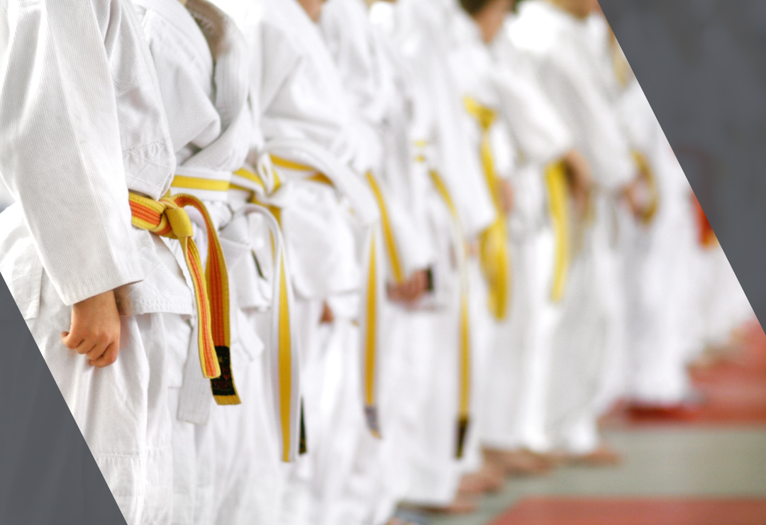 Karate students in white uniforms and yellow belts stand in a line during practice.