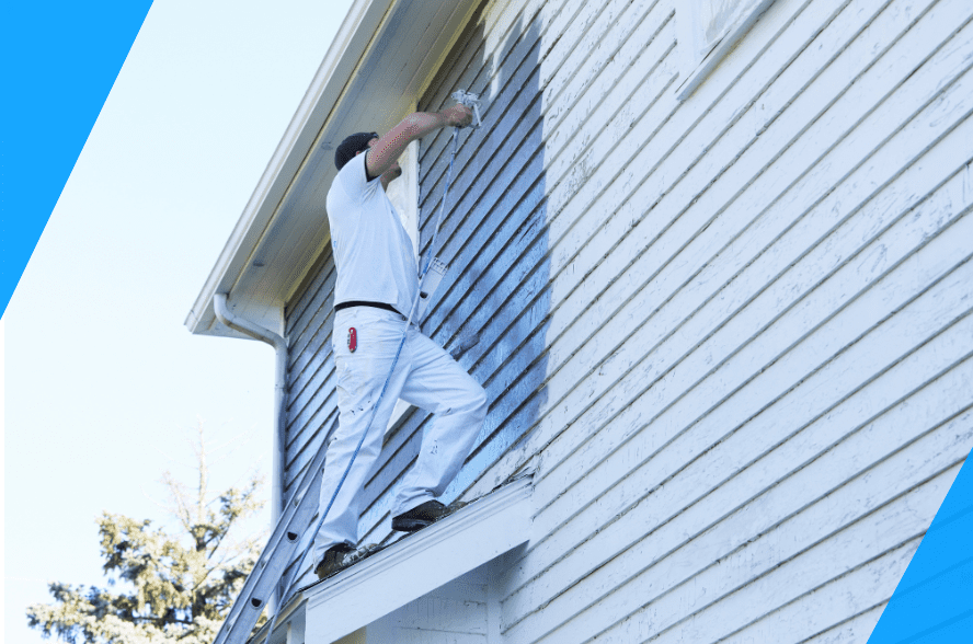 Man painting the exterior of a house with white paint, standing on a ladder.