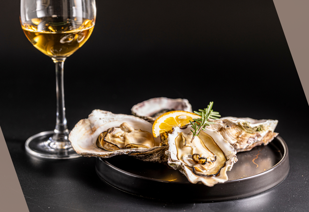 Plate of oysters with lemon and rosemary, accompanied by a glass of white wine.