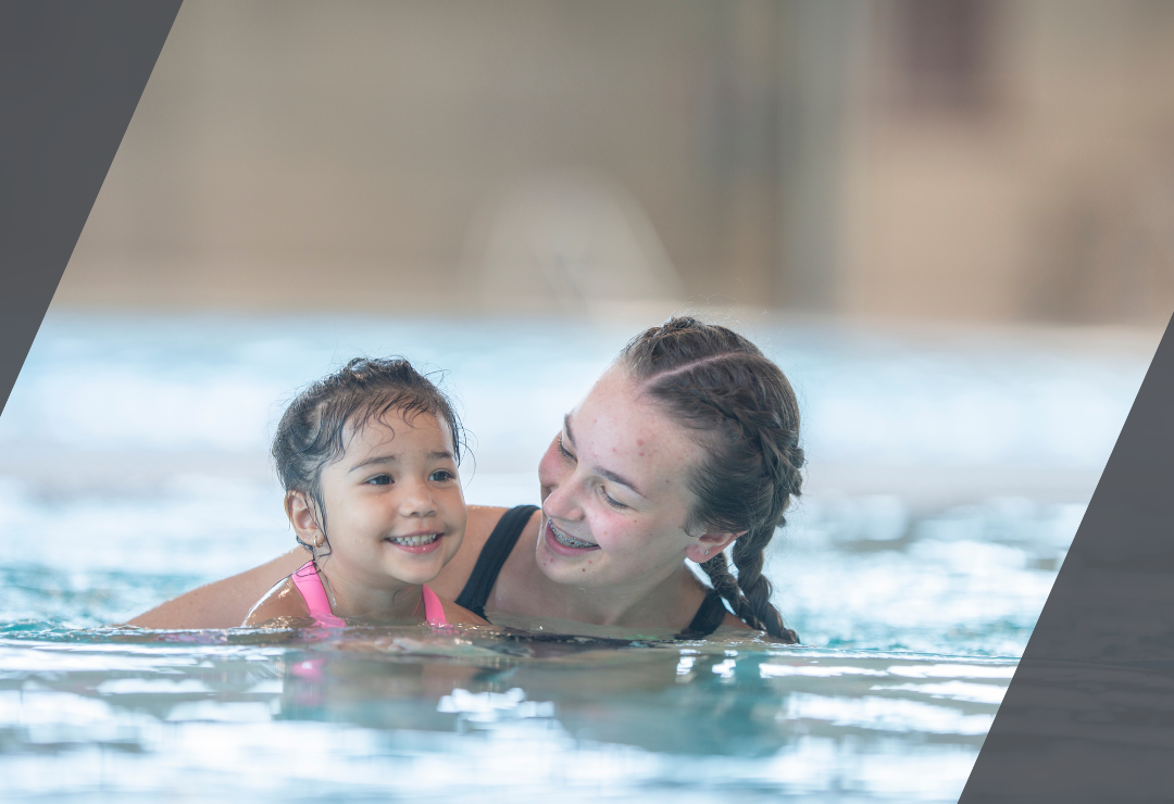A woman and child smiling while swimming together in a pool.