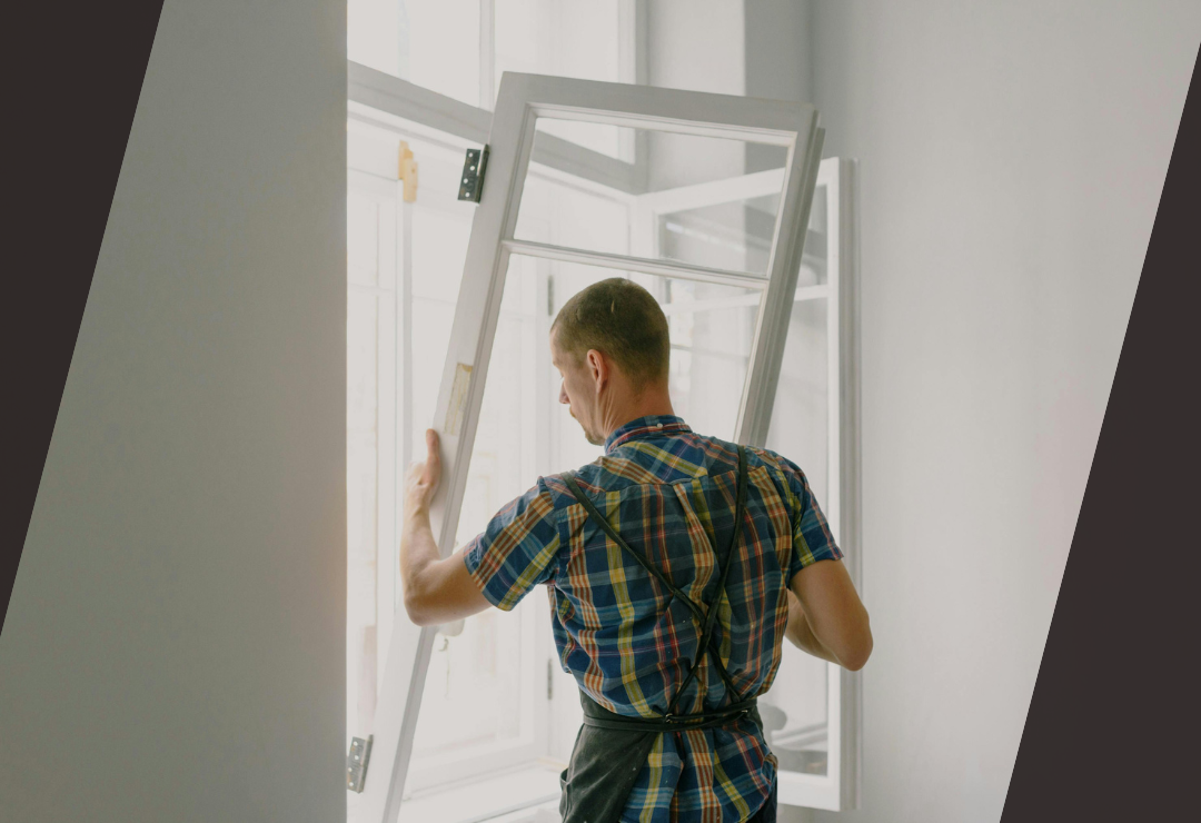 Man in plaid shirt installing or adjusting a window frame indoors.