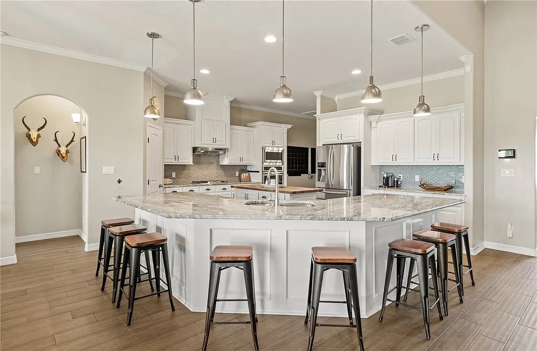 Spacious kitchen with a large marble island, bar stools, and modern appliances.