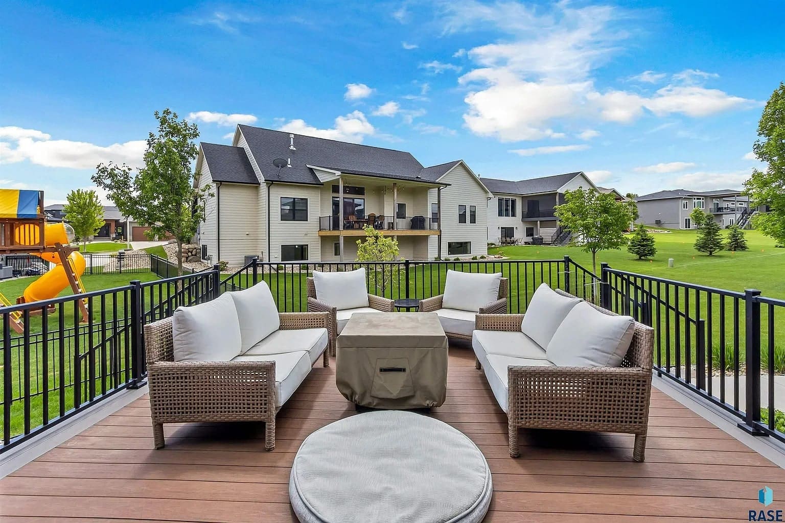 Outdoor patio with wicker furniture, fire pit, and view of suburban backyard and houses.