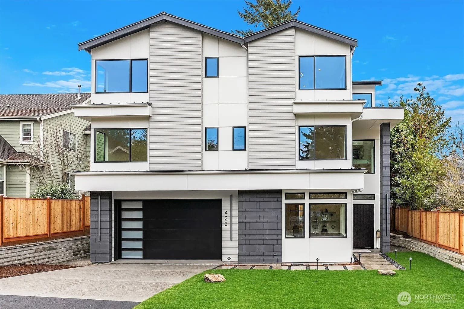 Modern three-story house with large windows, gray and white exterior, and a black garage door.