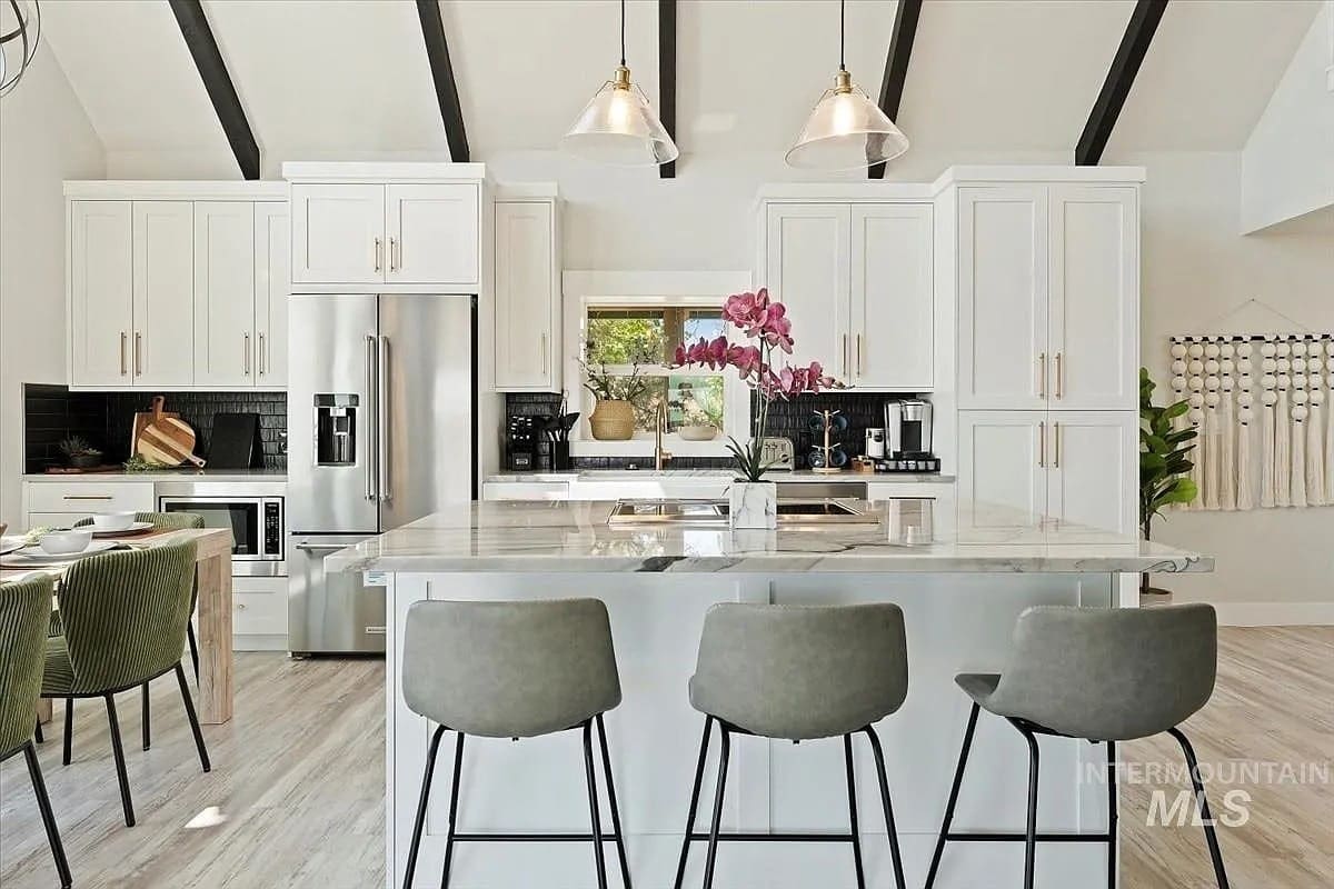 Modern kitchen with white cabinets, marble island, and gray barstools. Hanging lights and orchid centerpiece.
