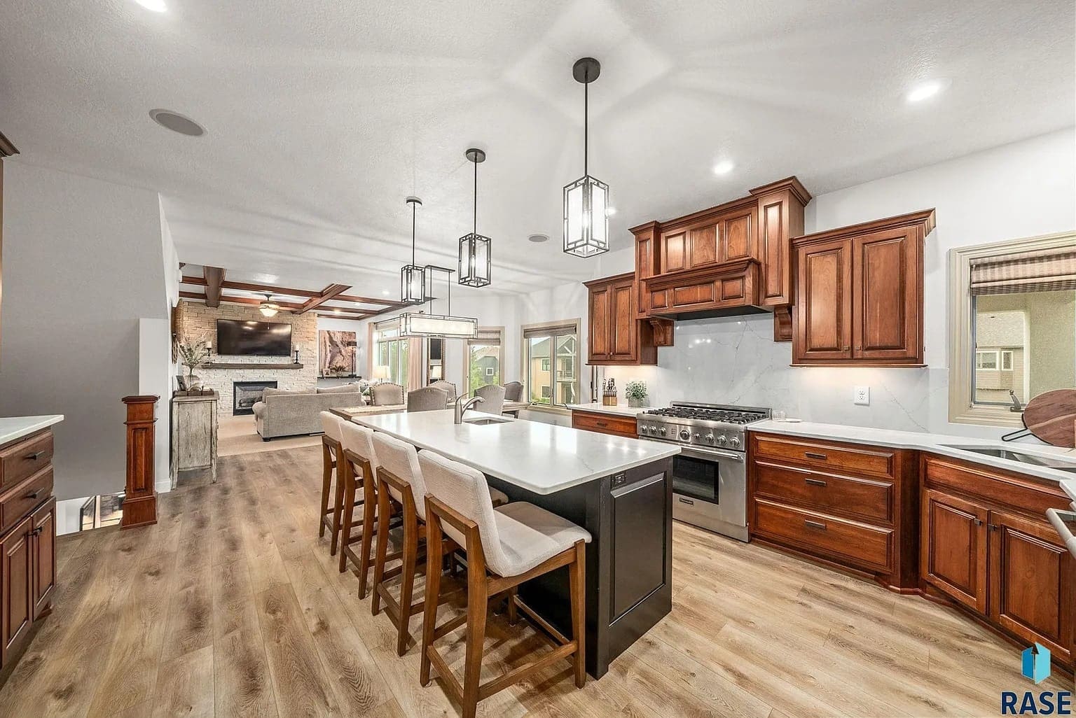Spacious modern kitchen with wooden cabinets, large island, and open layout leading to living area.
