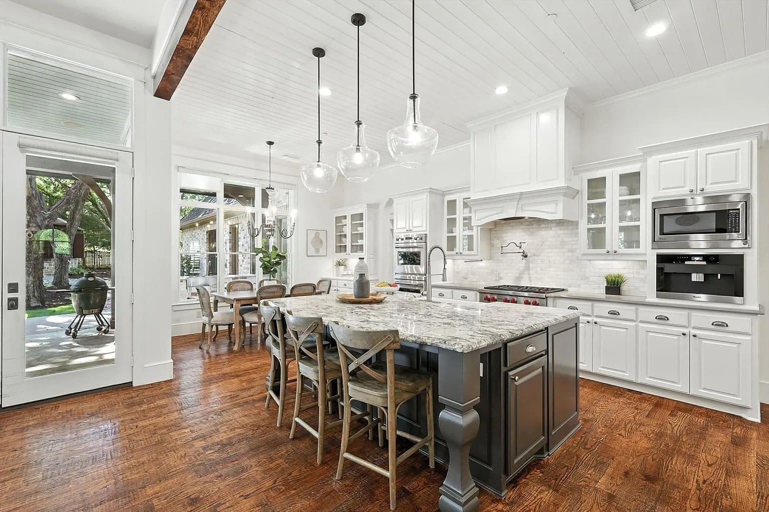 Spacious kitchen with a large island, pendant lights, and white cabinetry, overlooking a dining area.
