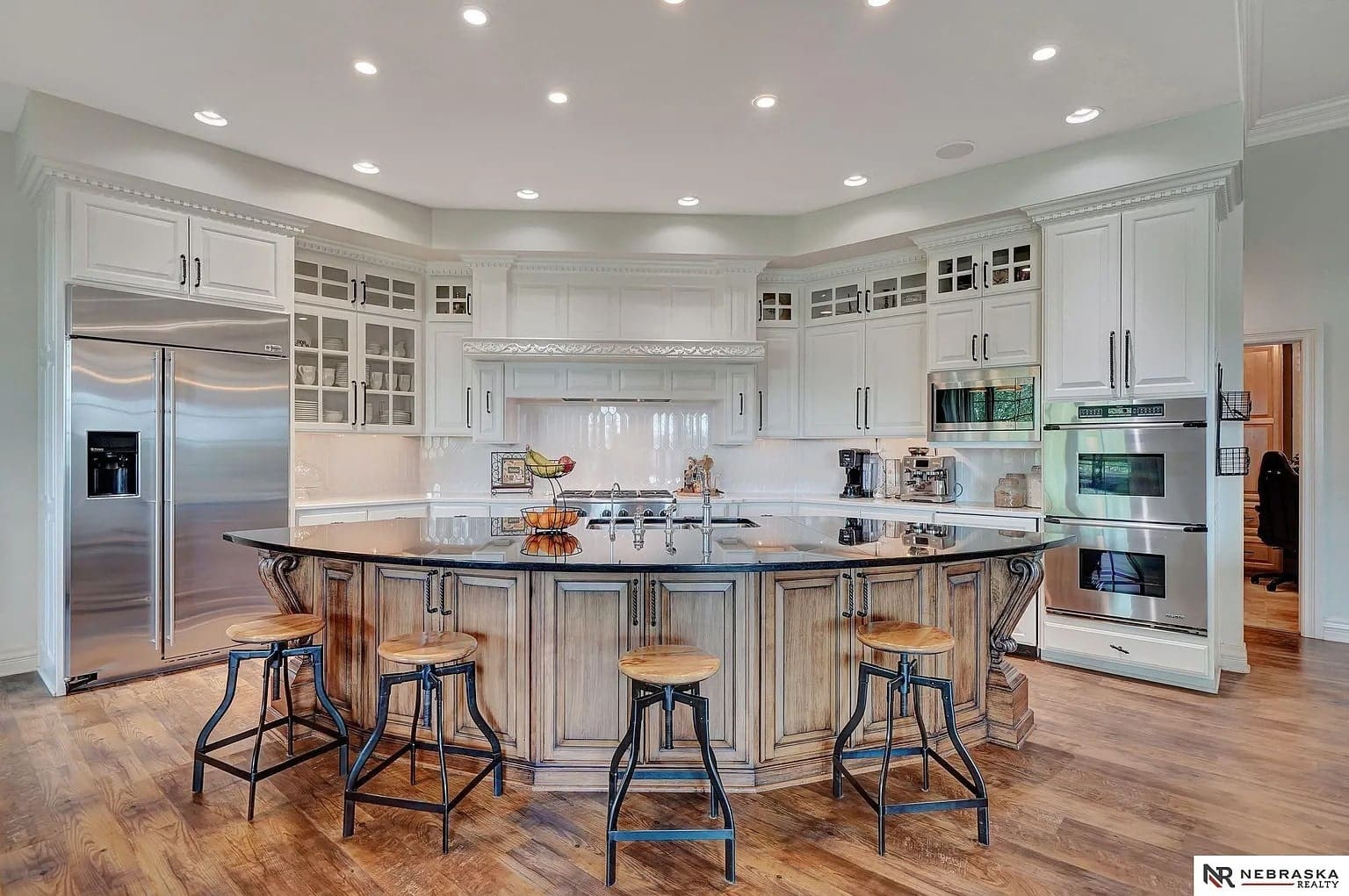 Spacious modern kitchen with a large island, bar stools, stainless steel appliances, and wooden flooring.