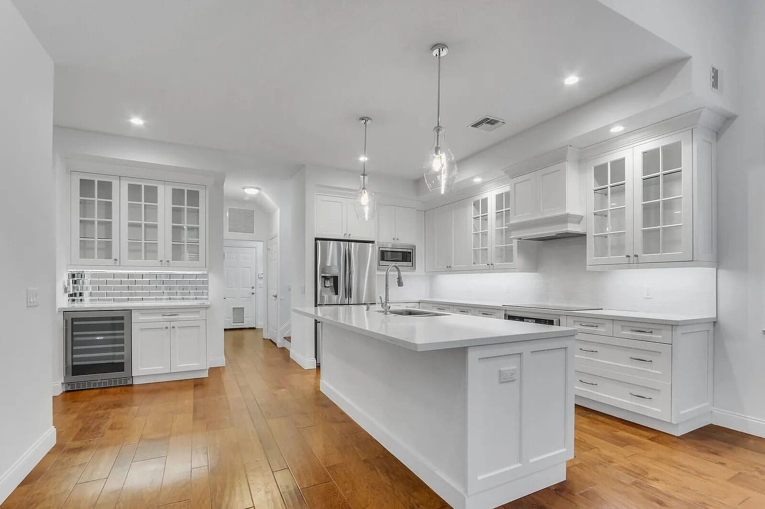 Modern kitchen with white cabinets, stainless steel appliances, and wooden floors.