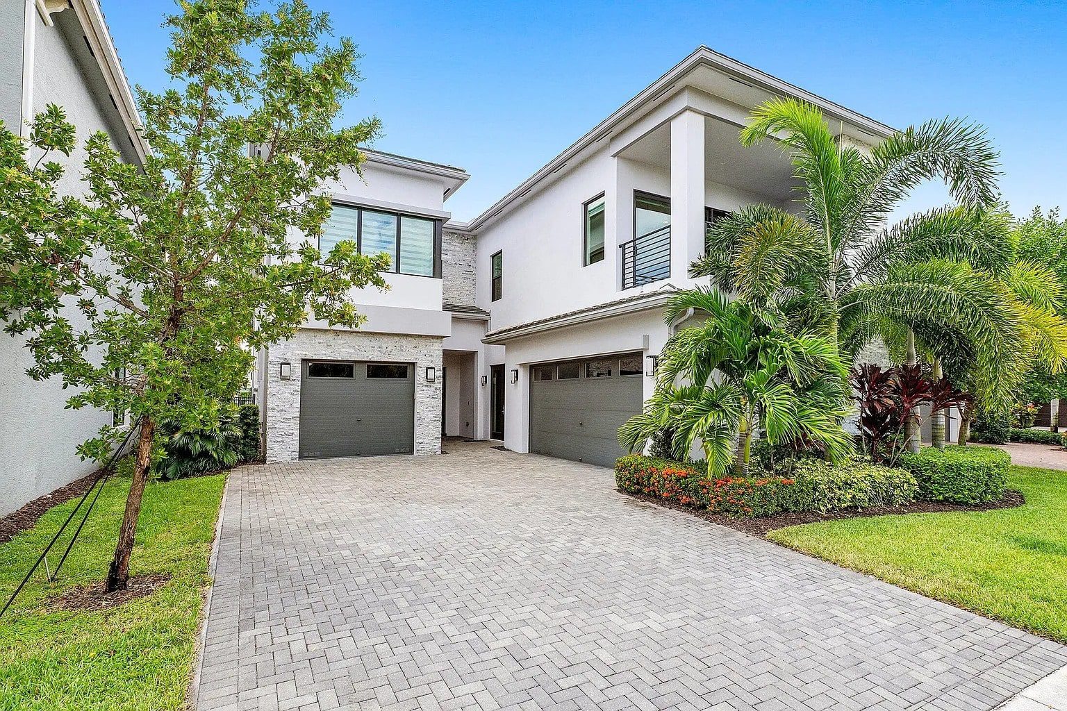 Modern two-story white house with a three-car garage, surrounded by palm trees and greenery.