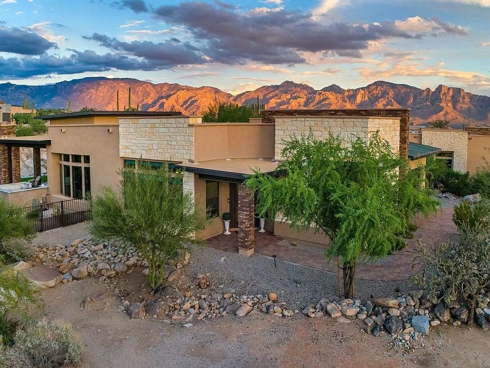 Modern desert home with stone accents, surrounded by rocky landscape and mountains in the background.