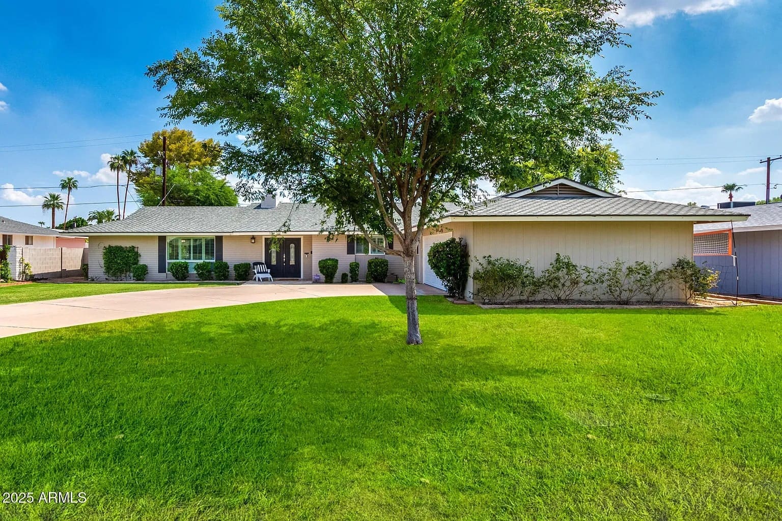 Single-story house with a green lawn, large tree, and a curved driveway in front.