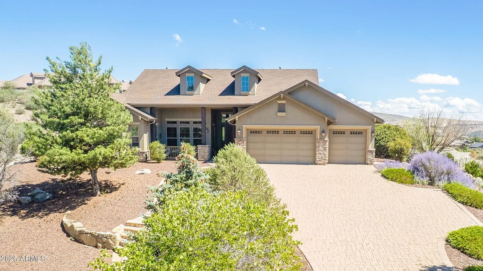 Large suburban house with a three-car garage, surrounded by trees and a brick driveway.