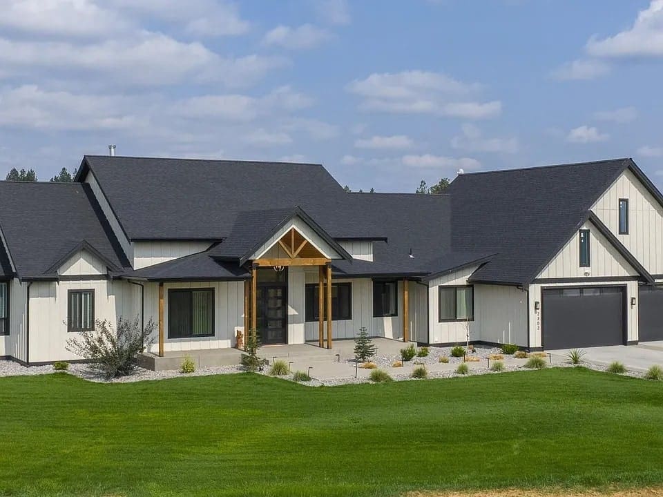 Modern farmhouse with black roof, white siding, large garage, and landscaped lawn under a blue sky.