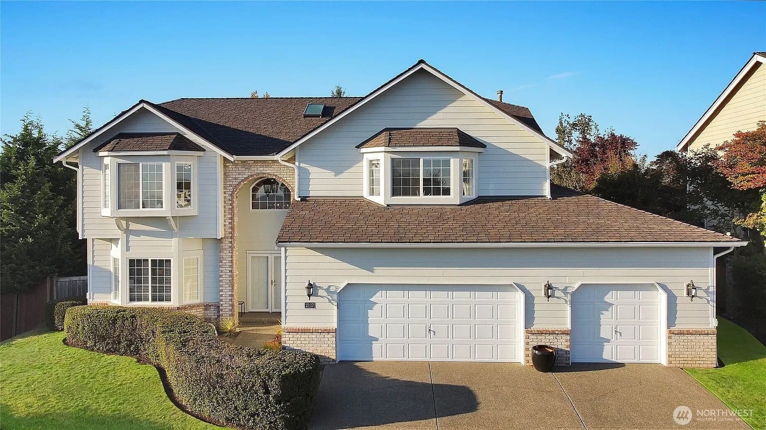 Two-story suburban house with a three-car garage and well-maintained lawn.