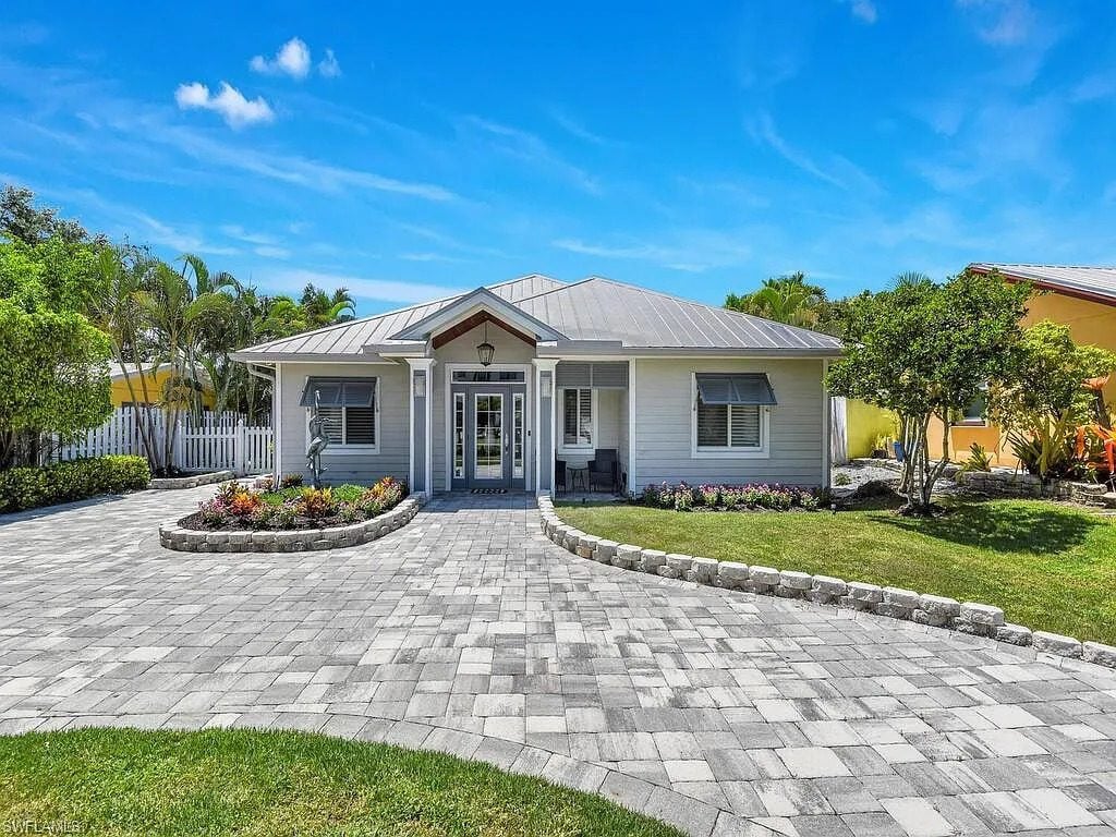 Single-story house with a metal roof, paved driveway, and landscaped front yard under a clear blue sky.