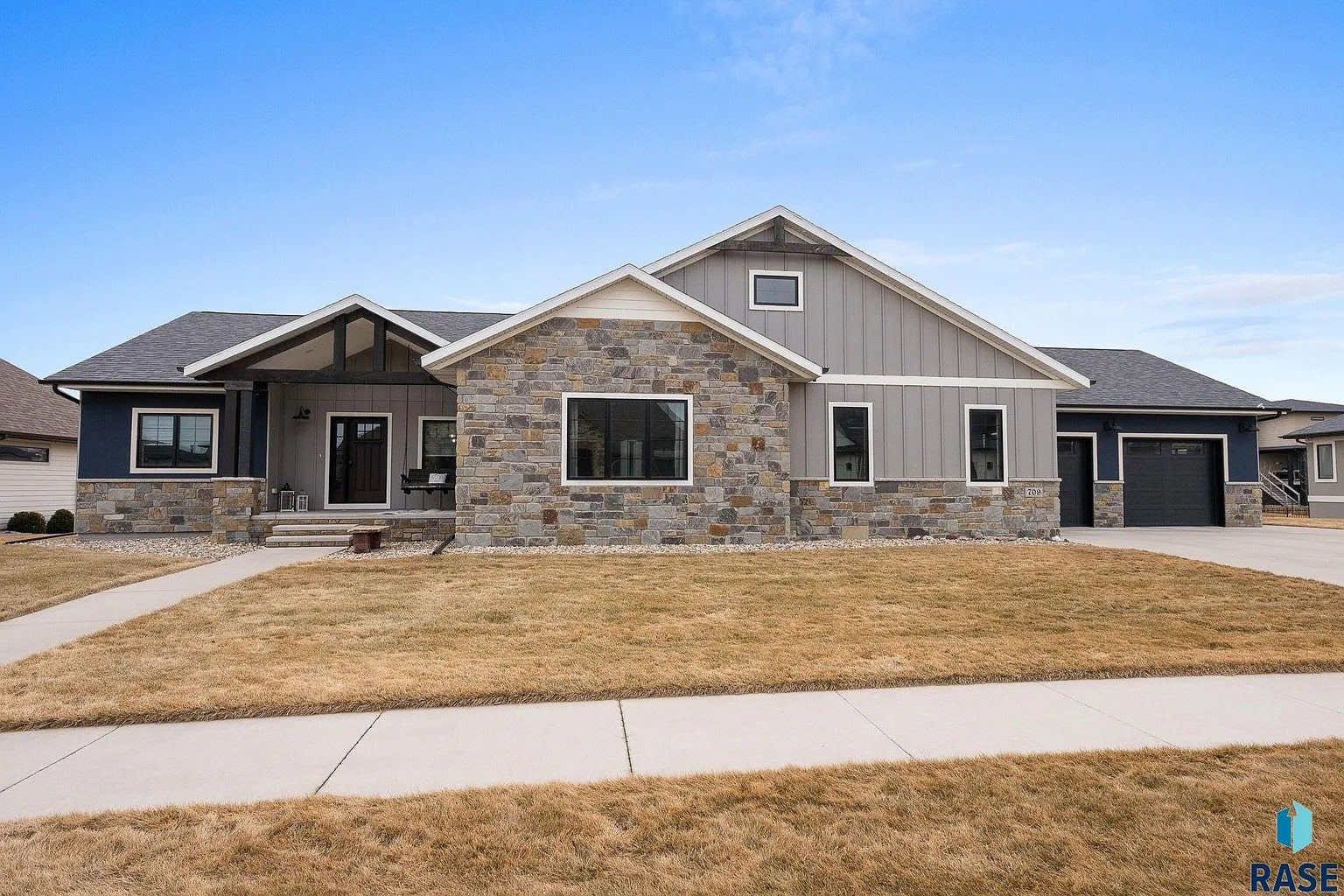 Single-story modern house with stone and siding exterior, large windows, and a covered porch.