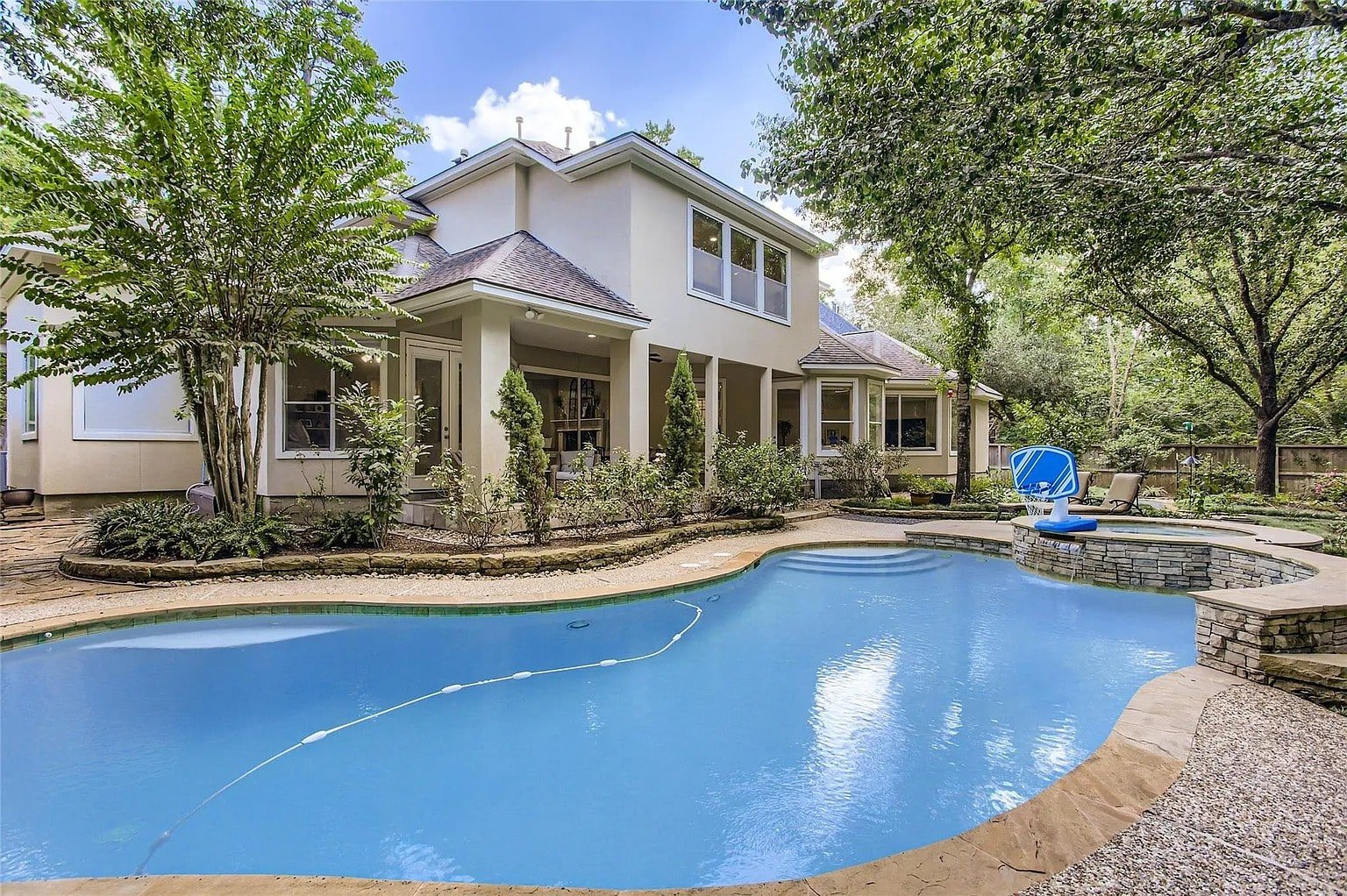 Backyard view of a house with a swimming pool, surrounded by trees and greenery.