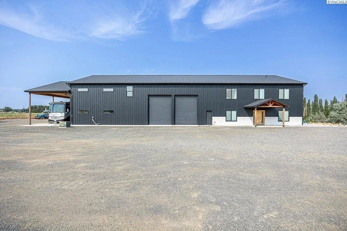 Large black industrial building with two garage doors and a gravel parking area in front.