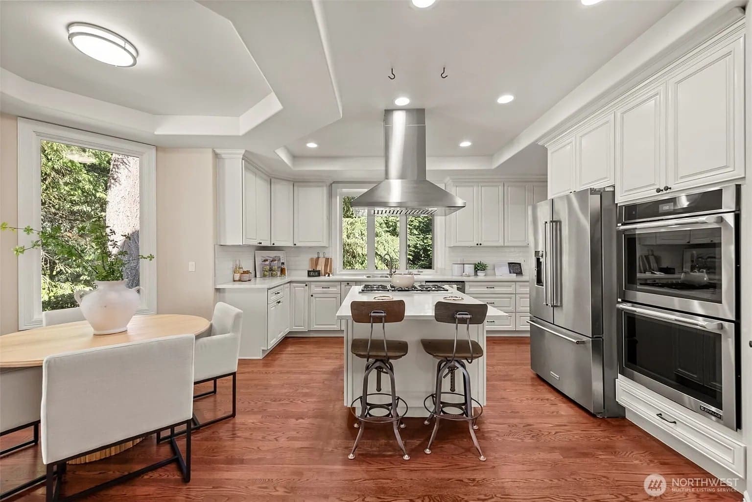 Modern kitchen with white cabinets, stainless steel appliances, island with bar stools, and a dining table.