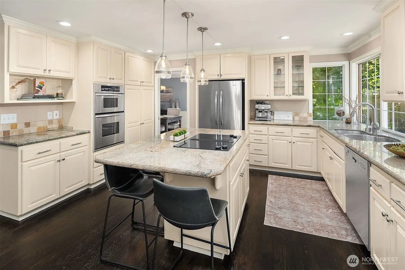Modern kitchen with white cabinets, granite countertops, island with bar stools, and stainless steel appliances.