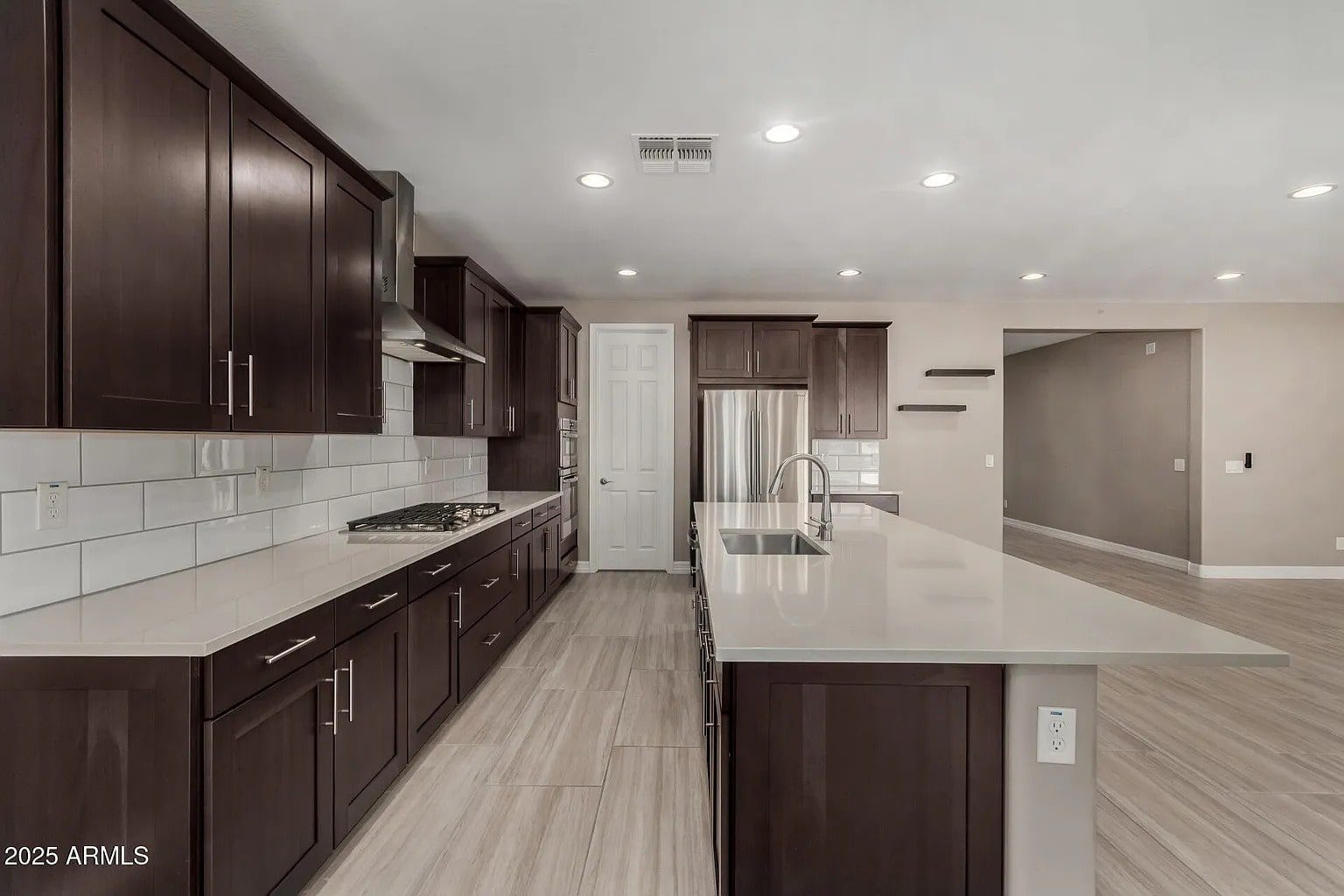 Modern kitchen with dark wood cabinets, white countertops, stainless steel appliances, and a large island.