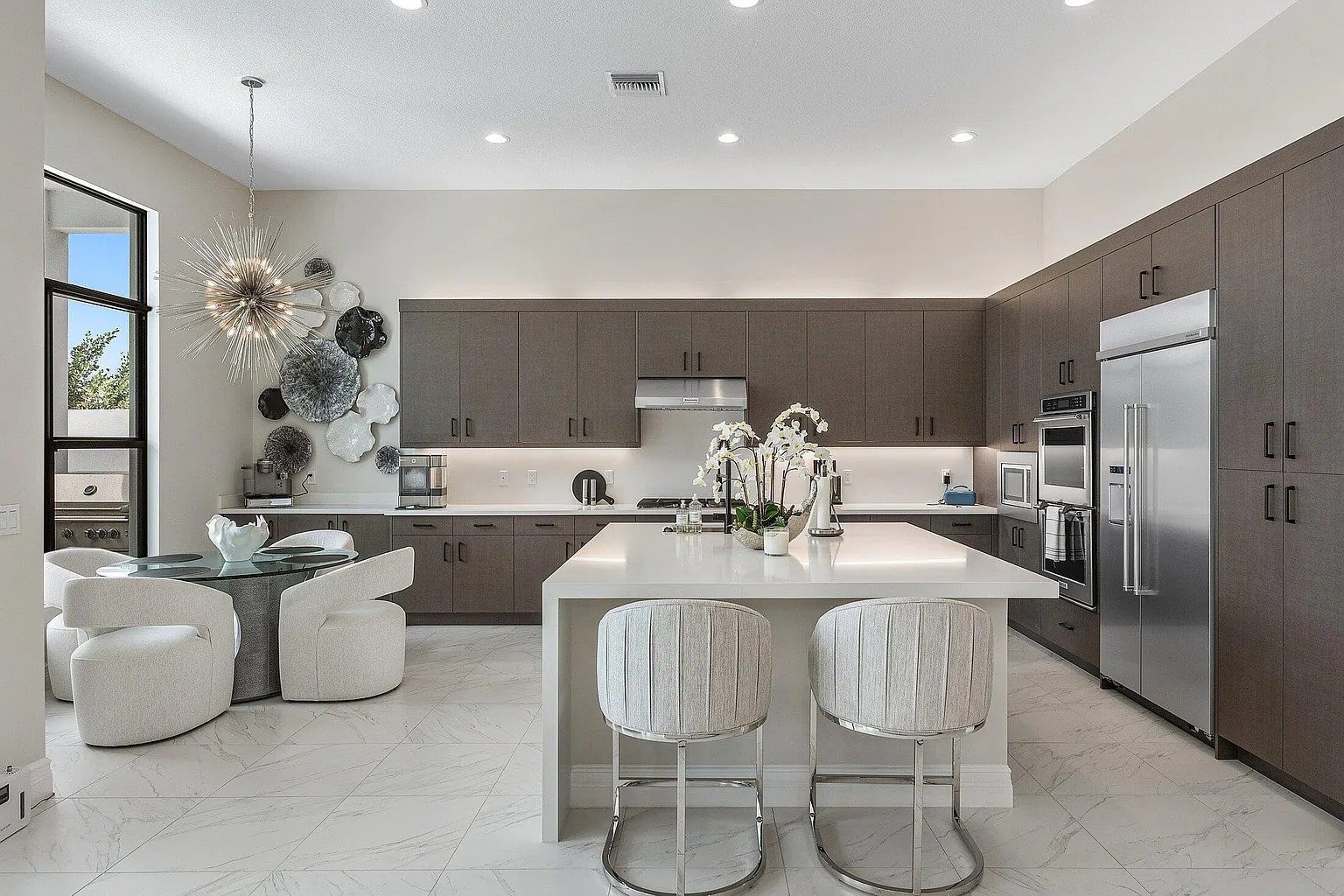 Modern kitchen with dark cabinets, large island, stainless steel appliances, and a round dining table.