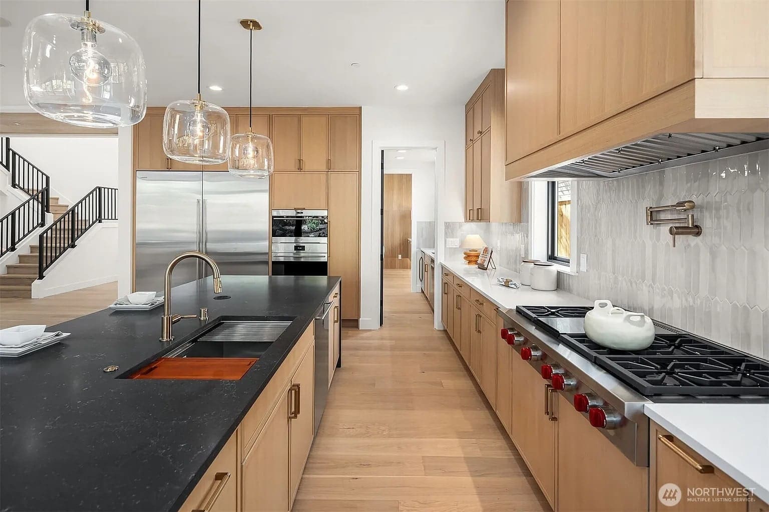 Modern kitchen with wooden cabinets, black island countertop, stainless steel appliances, and pendant lights.