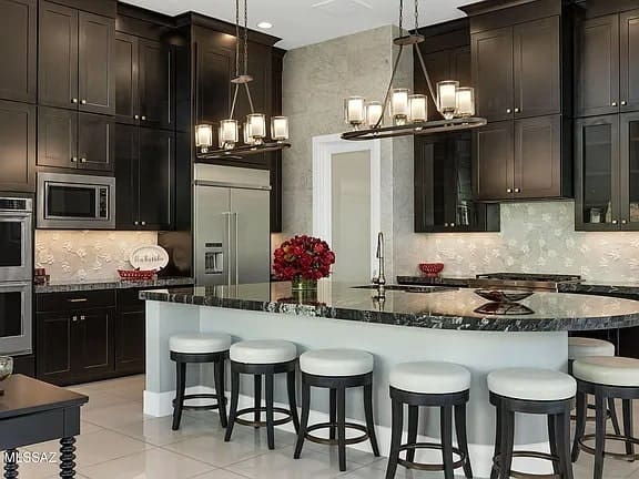 Modern kitchen with dark cabinets, marble countertops, and bar stools around an island.