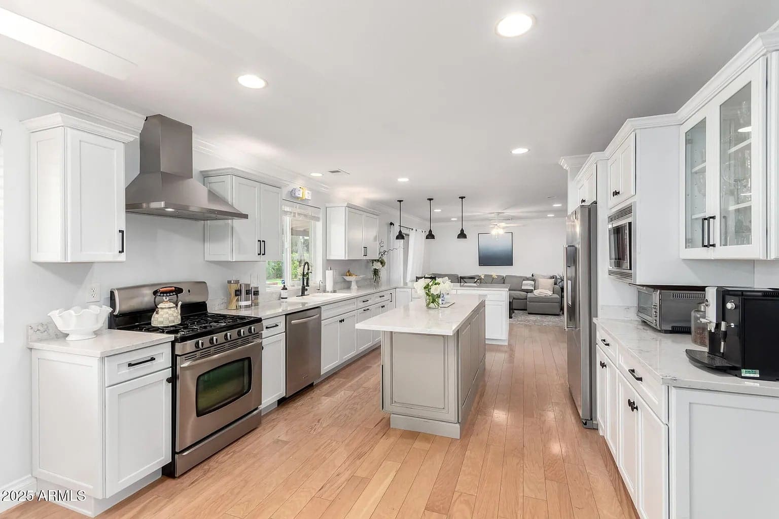 Modern kitchen with white cabinets, stainless steel appliances, and a central island. Open layout to living area.