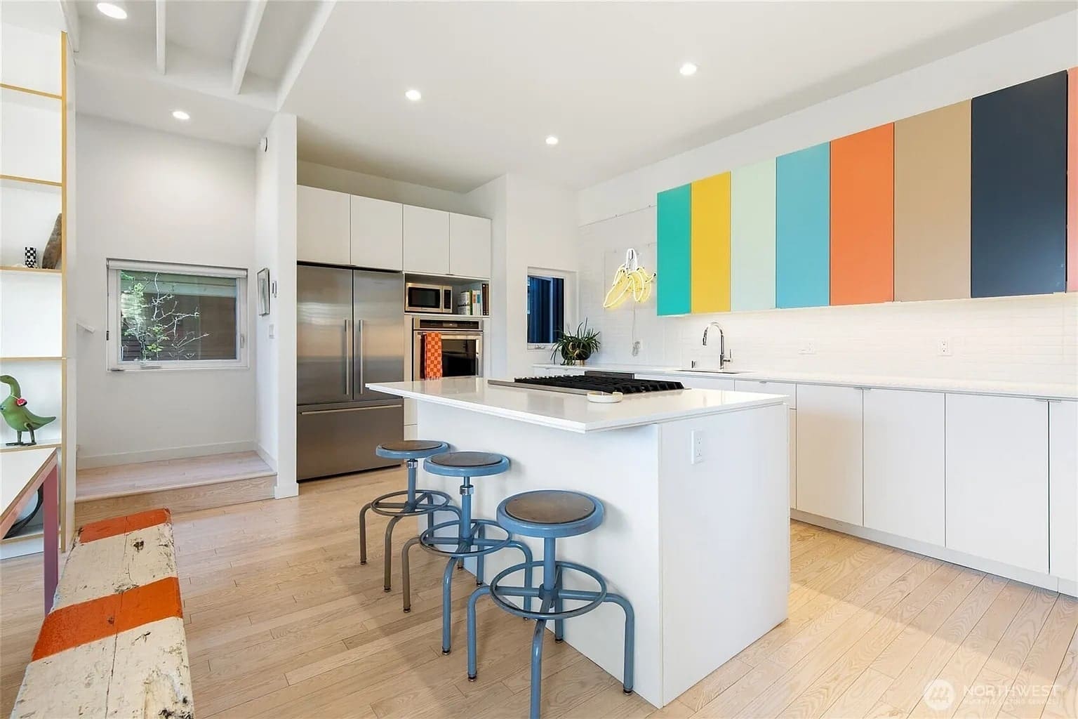Modern kitchen with colorful cabinets, white island, stainless steel appliances, and bar stools.