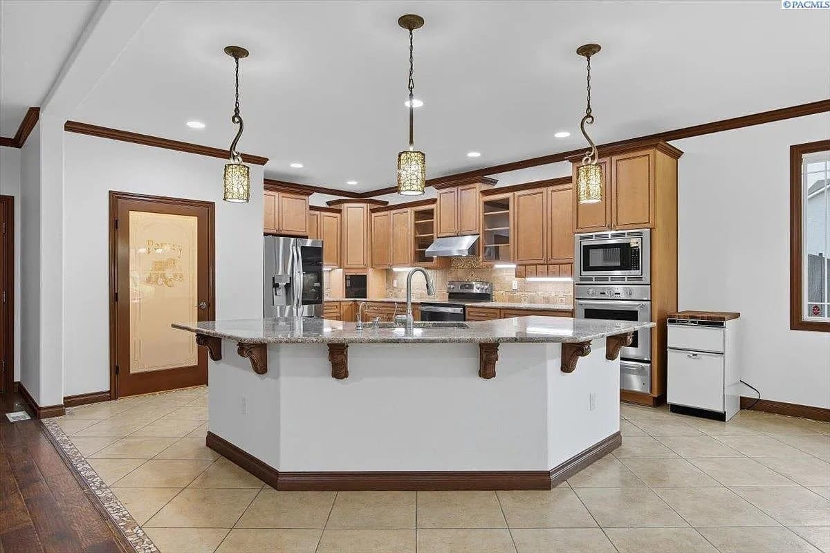 Spacious kitchen with wooden cabinets, large island, stainless steel appliances, and pendant lighting.