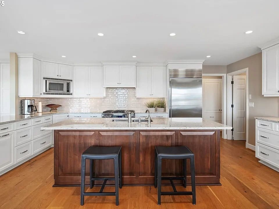 Modern kitchen with white cabinets, stainless steel appliances, and a large wooden island with stools.
