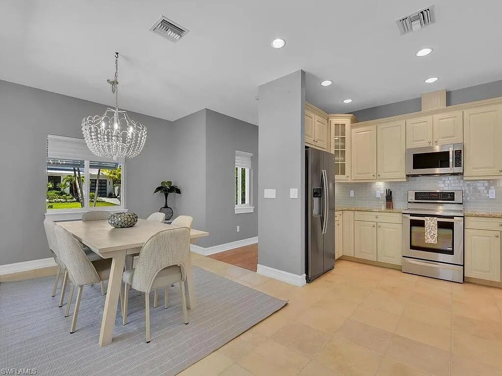 Modern kitchen and dining area with light gray walls, beige cabinets, and a chandelier over the table.