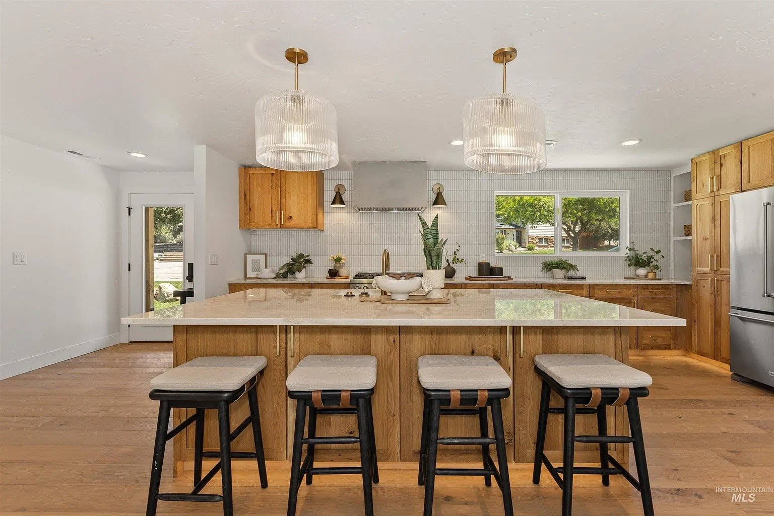 Modern kitchen with a large island, bar stools, pendant lights, and wooden cabinets.