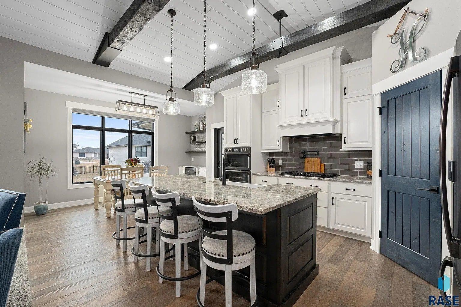 Modern kitchen with a large island, white cabinets, dark beams, and pendant lighting.