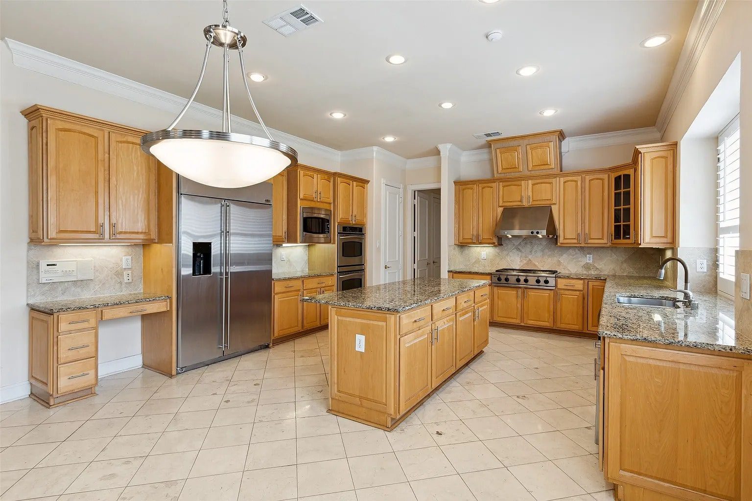 Spacious kitchen with wooden cabinets, granite countertops, island, stainless steel appliances, and tile flooring.