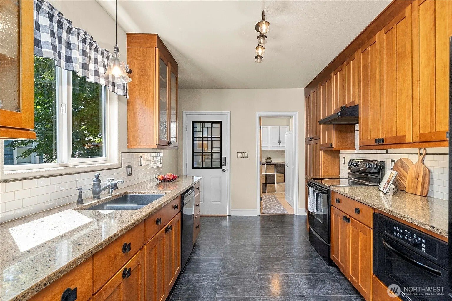 Galley kitchen with wooden cabinets, granite countertops, and stainless steel appliances. Door leads to another room.