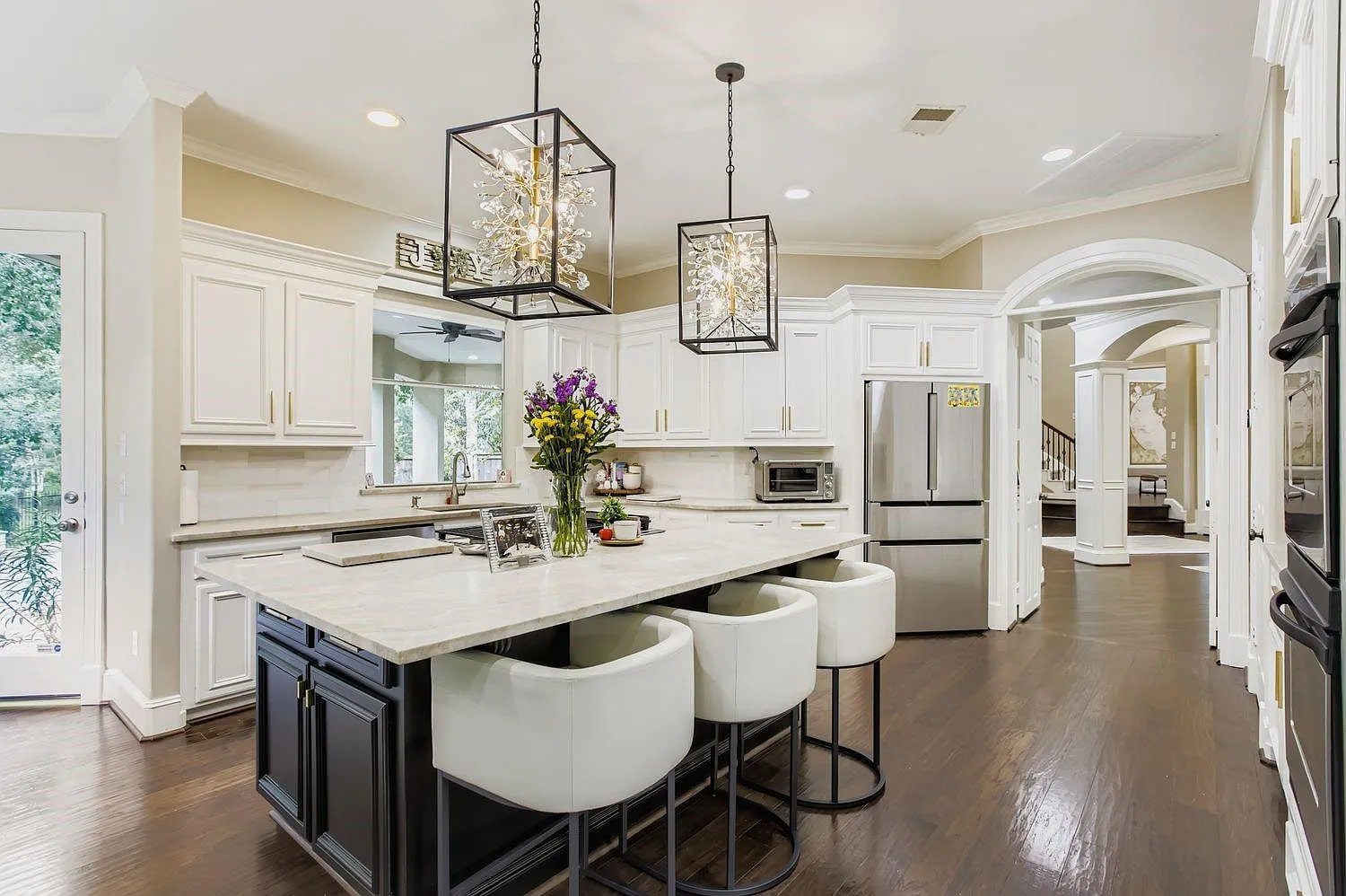 Modern kitchen with white cabinets, island with barstools, stainless steel appliances, and decorative lighting.