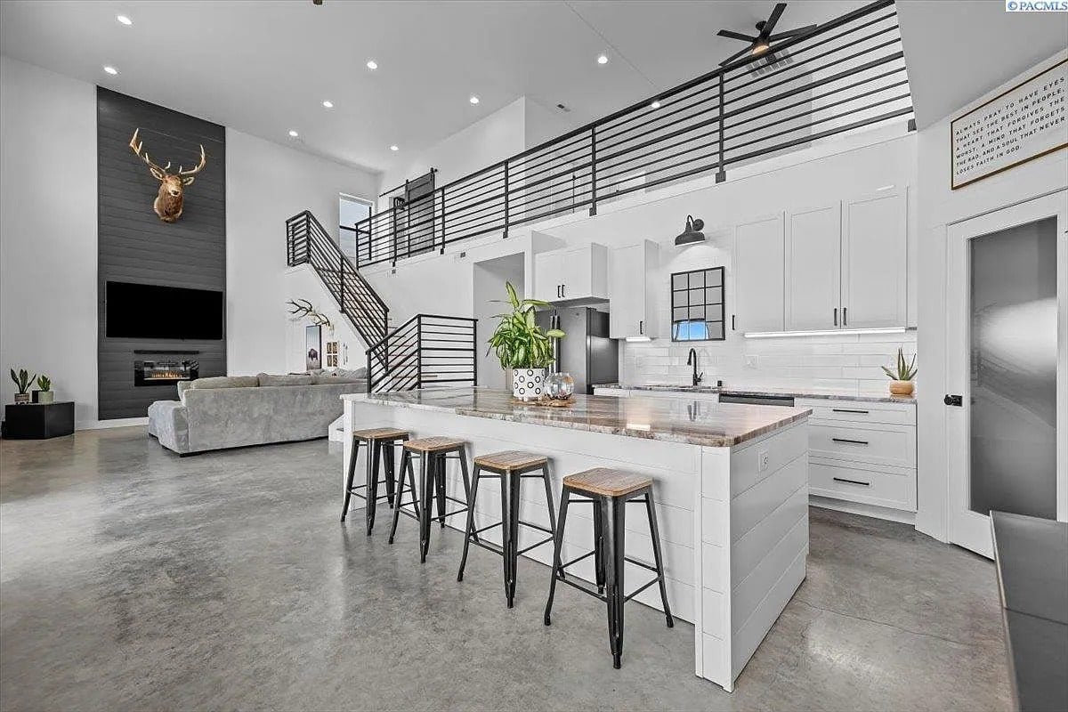 Modern open-concept kitchen with white cabinets, island seating, and high ceilings. Loft and living area visible.