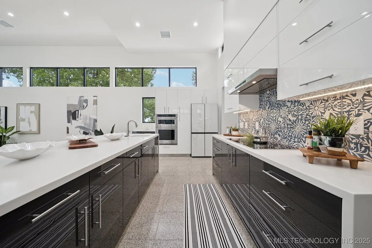 Modern kitchen with sleek black and white cabinets, patterned backsplash, and large windows.