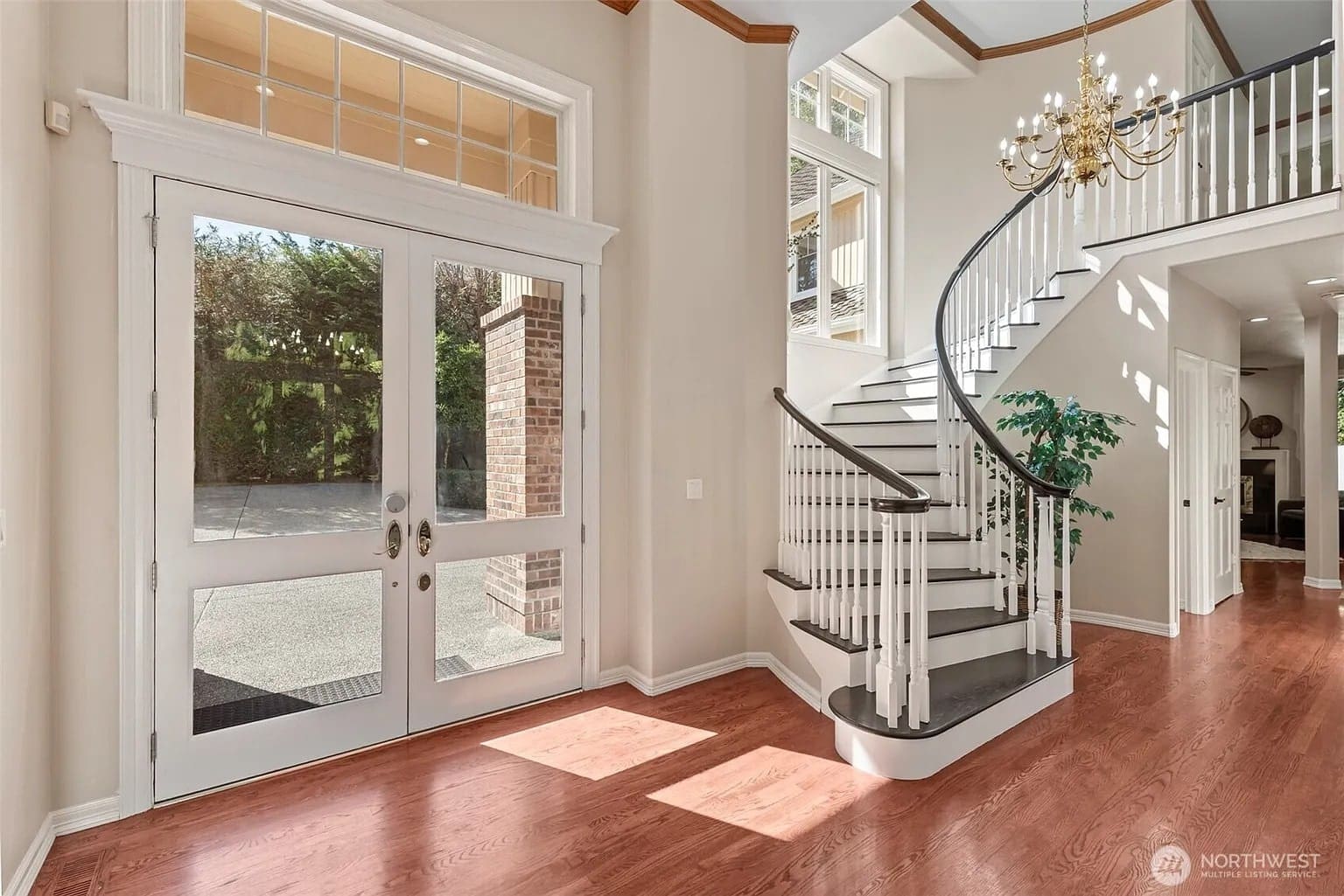 Spacious foyer with curved staircase, chandelier, and large glass doors leading outside.