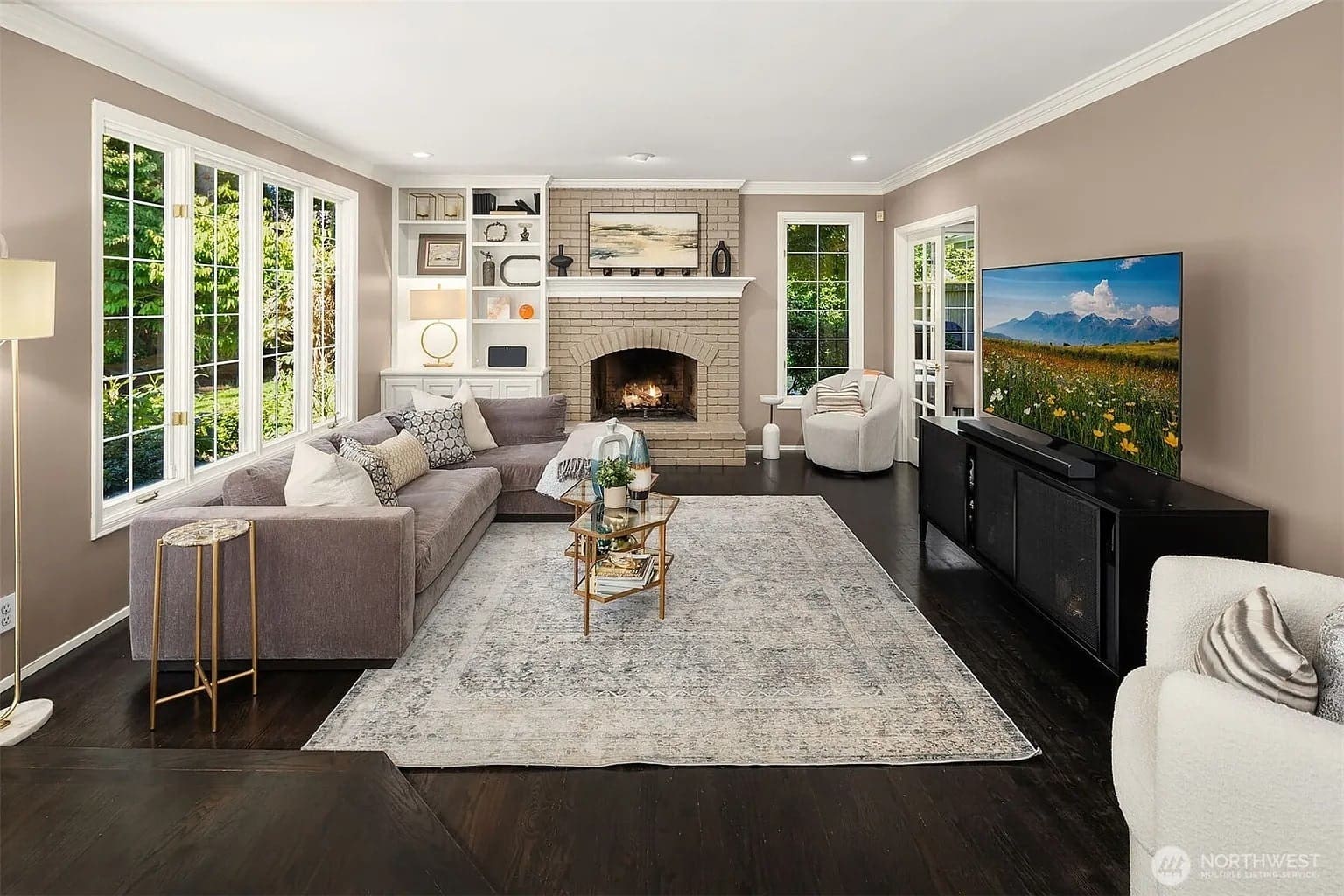 Spacious living room with a fireplace, large windows, gray sectional sofa, and a TV on a console.
