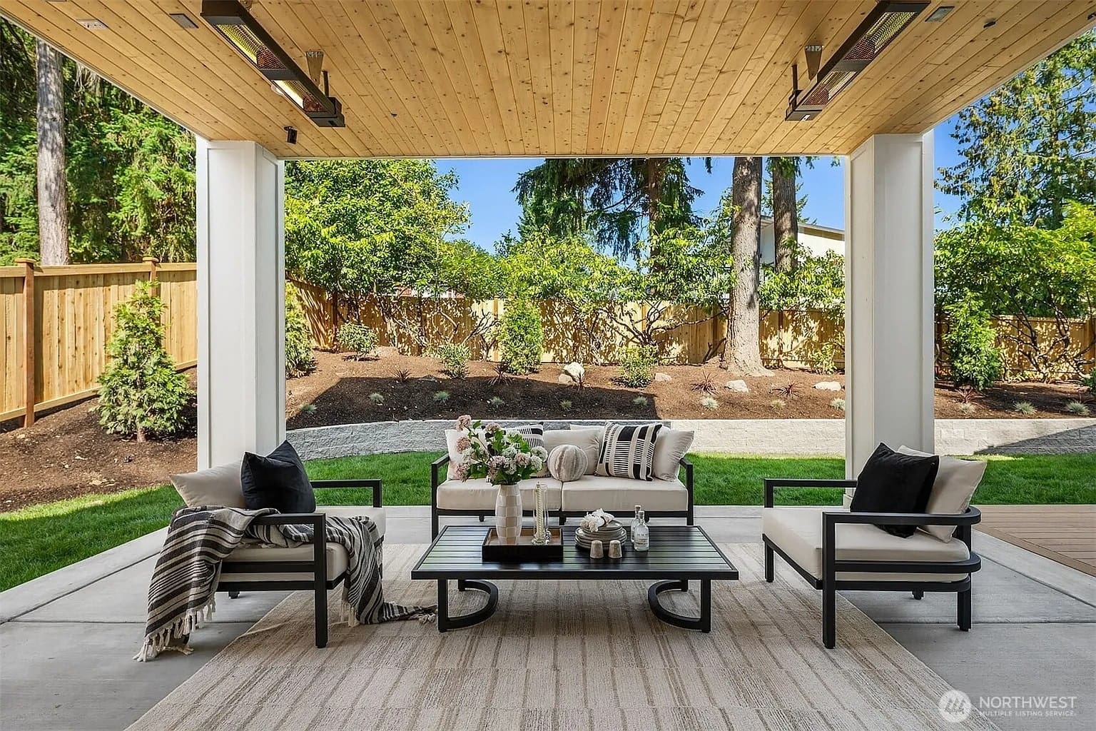Covered outdoor patio with modern furniture, rug, and garden view.