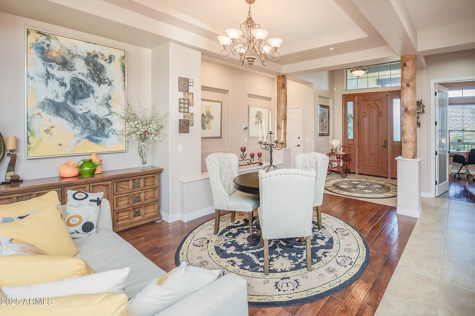 Elegant living room with a round dining table, chandelier, and abstract artwork on the wall.