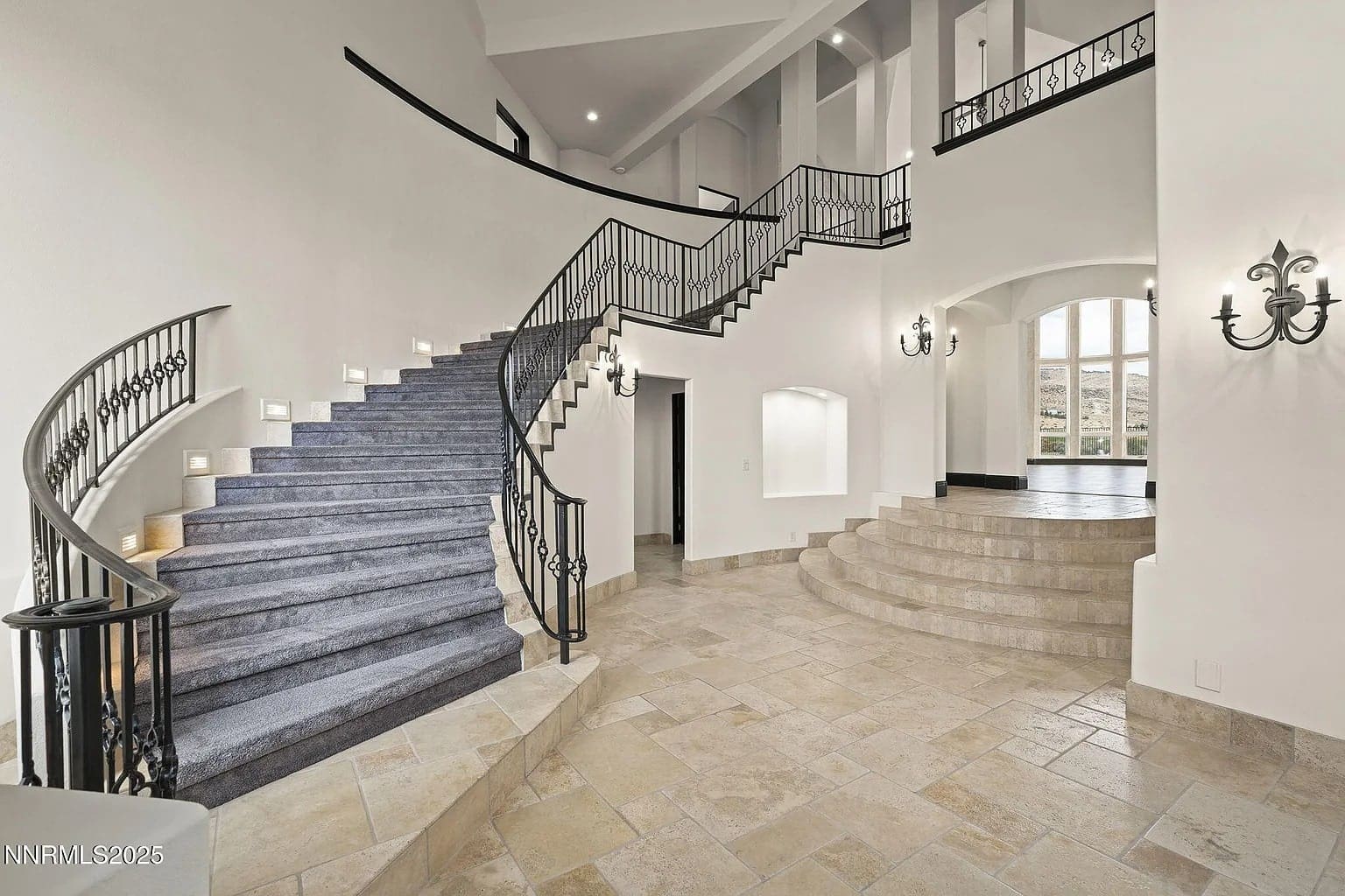 Spacious foyer with elegant curved staircase, tiled floors, and wrought iron railings.